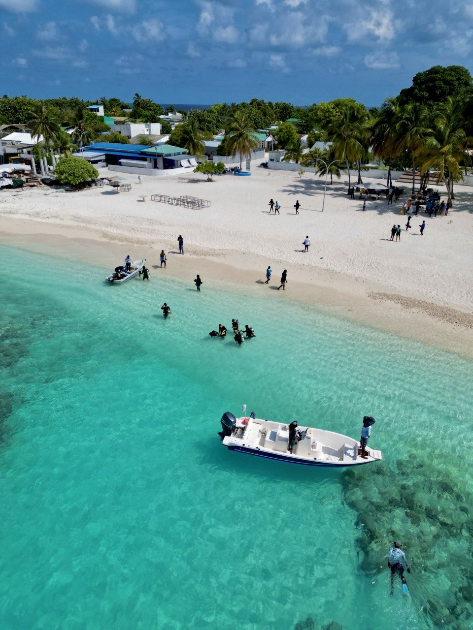 Aerial view of boats, swimmers and community activity along Dharavandhoo beach