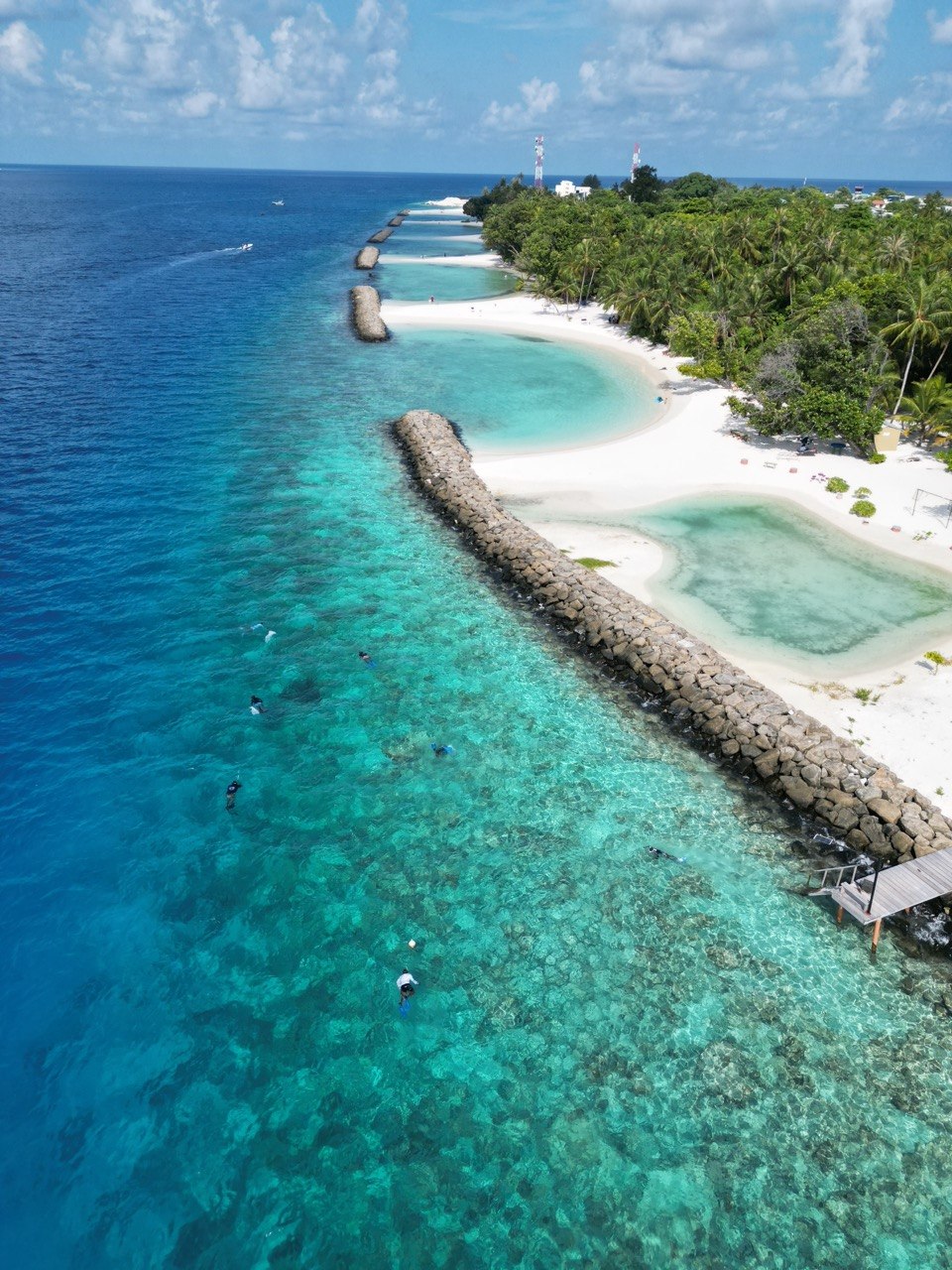 Aerial view along Dharavandhoo's white shoreline, reef edge and clear lagoon