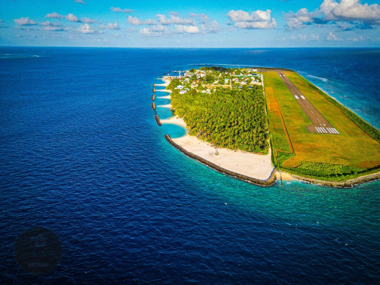 Wide aerial view of Dharavandhoo island, its runway, shoreline and surrounding reef